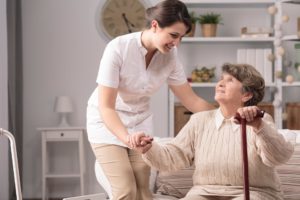 photo of caregiver helping elderly woman with a cane get up from sitting