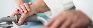 close-up photo of elderly person's hands on a walker with nurse touching one hand